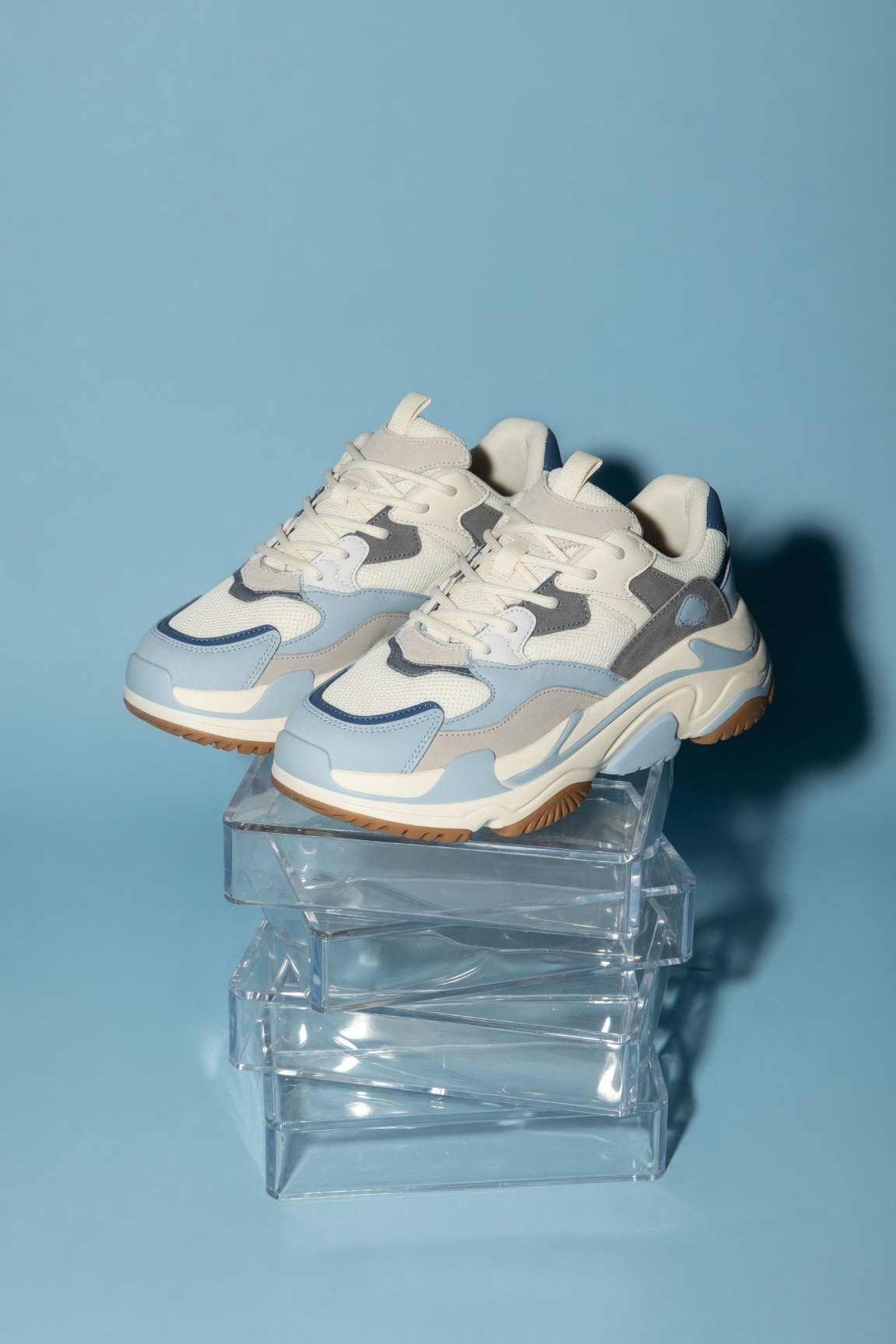 Zapatillas chunky celestes y crema apoyadas sobre cajas de acrílico