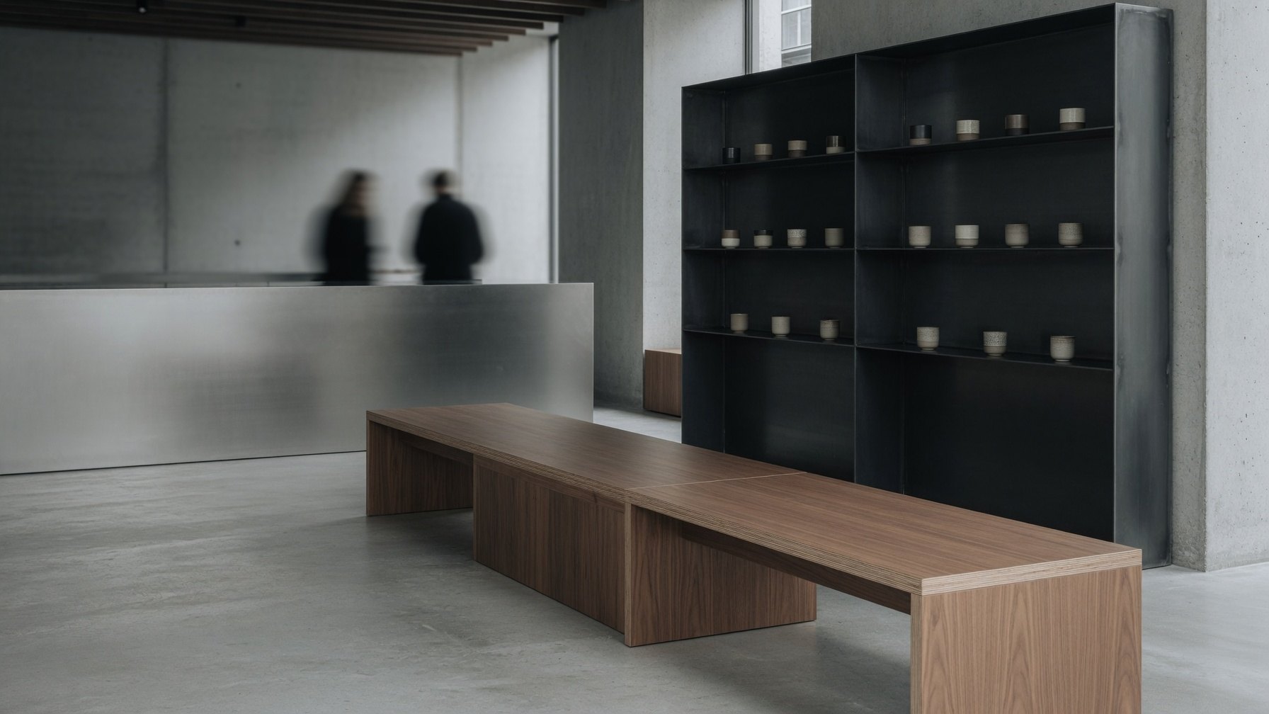 Salón minimalista con banco largo de madera, piso de hormigón pulido y estantería de acero negro con tazas de cerámica
